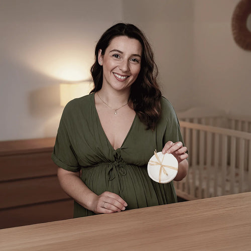 Mamá sonriendo muestra par de absorbentes de leche ecológicos Bambú Contour de Pequelandia en dormitorio infantil